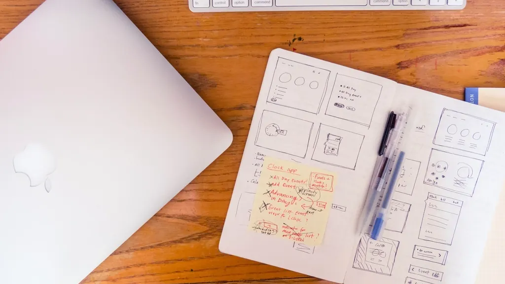 Cuaderno con bocetos de pantallas de una web junto a un portátil cerrado